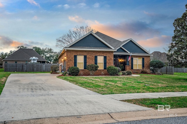 craftsman house featuring driveway, fence, a lawn, and brick siding