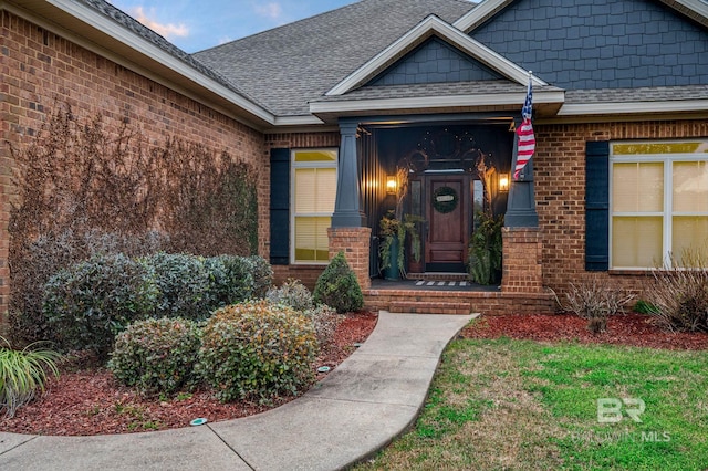 view of exterior entry with roof with shingles and brick siding