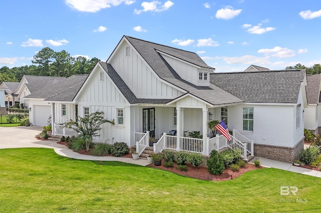 modern farmhouse featuring a front yard, driveway, brick siding, covered porch, and board and batten siding