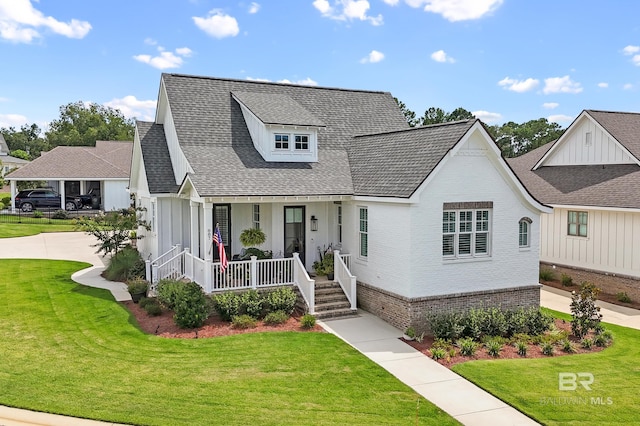 view of front facade featuring brick siding, covered porch, a front lawn, and roof with shingles