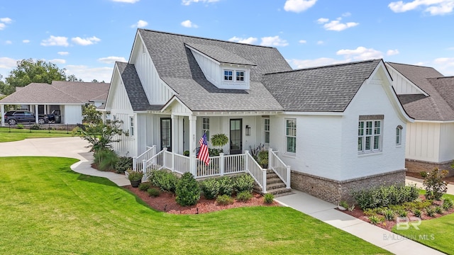 modern farmhouse featuring brick siding, covered porch, a front lawn, and roof with shingles