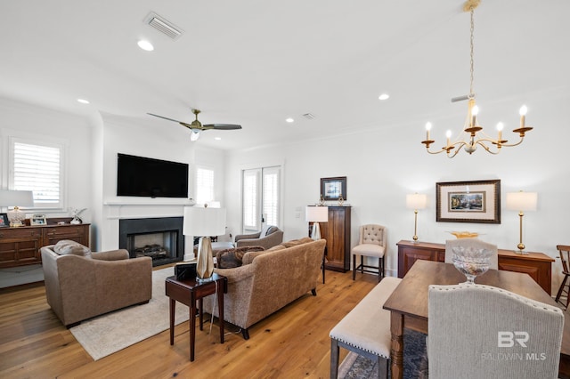 living room featuring ornamental molding, ceiling fan with notable chandelier, wood-type flooring, and a wealth of natural light