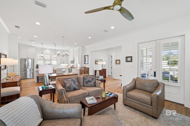 living room featuring light wood-type flooring, ceiling fan with notable chandelier, and ornamental molding