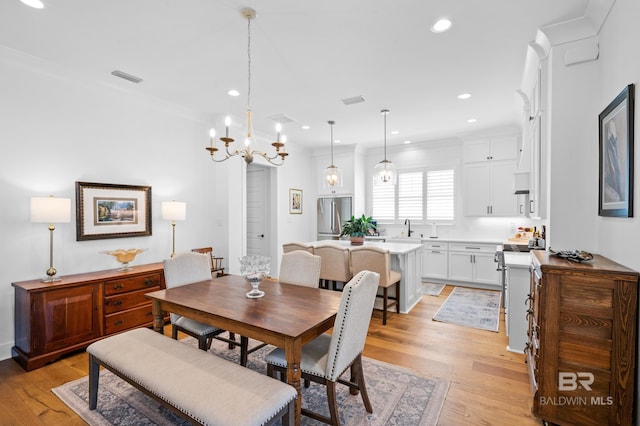 dining space with ornamental molding, a notable chandelier, light hardwood / wood-style flooring, and sink