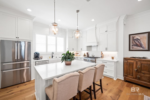 kitchen featuring white cabinetry, premium range hood, light wood-type flooring, a kitchen island, and appliances with stainless steel finishes