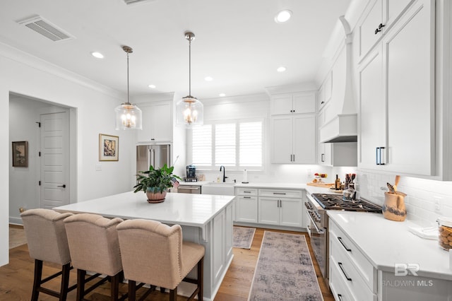 kitchen with light wood-type flooring, a center island, premium range hood, high quality appliances, and a kitchen bar