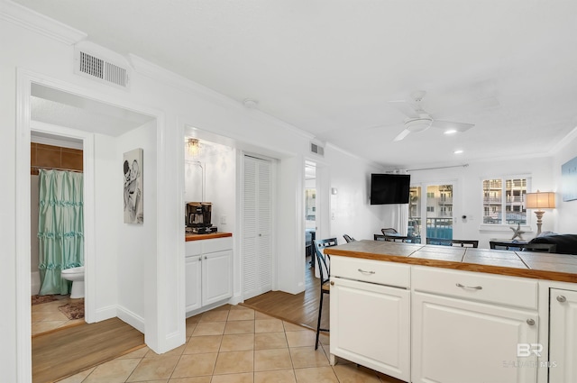 kitchen with light tile patterned floors, tile countertops, visible vents, white cabinets, and ceiling fan
