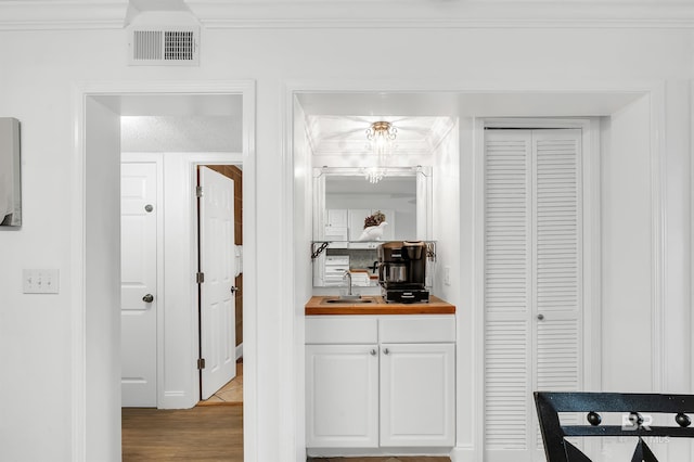 hall featuring a sink, ornamental molding, visible vents, and wood finished floors