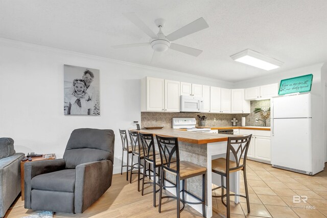 kitchen with light countertops, a peninsula, white appliances, a kitchen bar, and backsplash