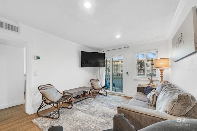 living room featuring baseboards, visible vents, crown molding, and wood finished floors