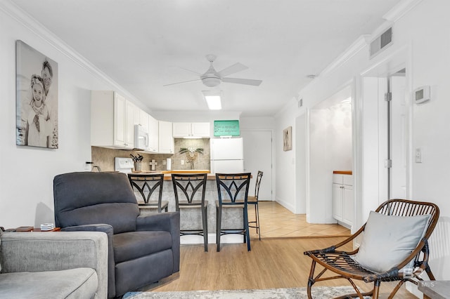living room featuring visible vents, light wood-style floors, ornamental molding, and a ceiling fan