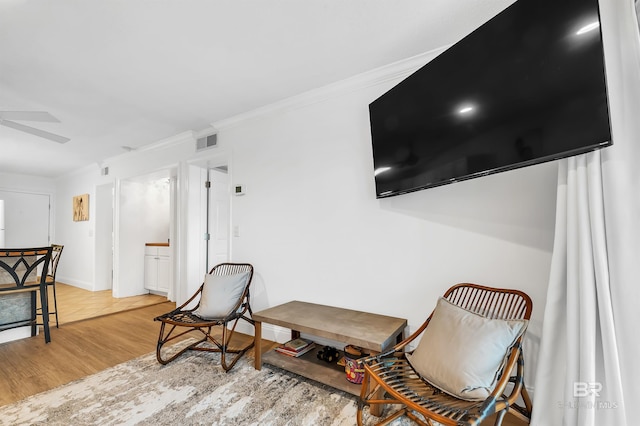sitting room featuring a ceiling fan, visible vents, crown molding, and wood finished floors