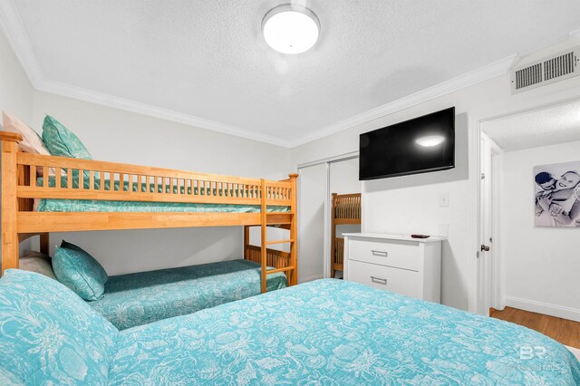 bedroom with wood finished floors, a textured ceiling, baseboards, visible vents, and ornamental molding