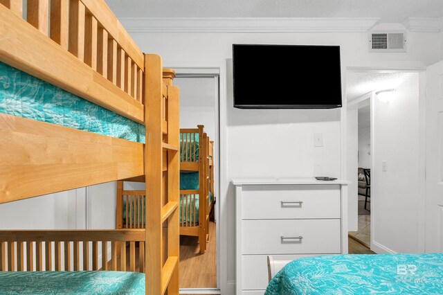 bedroom featuring visible vents, wood finished floors, and ornamental molding