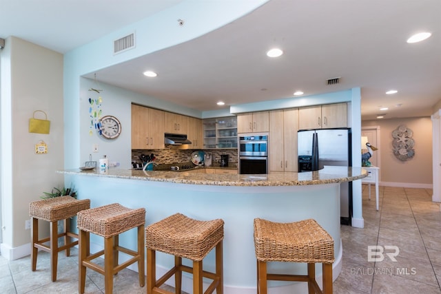 kitchen featuring light brown cabinetry, backsplash, light stone counters, kitchen peninsula, and stainless steel appliances