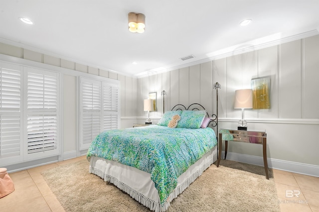 bedroom featuring a decorative wall, visible vents, baseboards, ornamental molding, and tile patterned floors