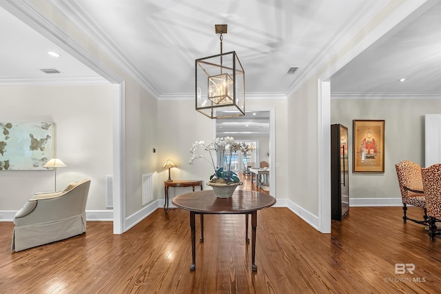 interior space featuring an inviting chandelier, wood-type flooring, visible vents, and crown molding