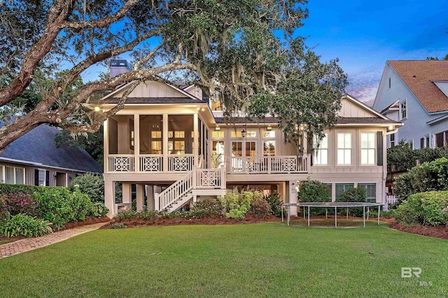 rear view of property with board and batten siding, a sunroom, stairs, and a lawn