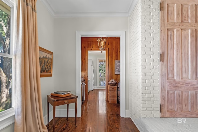 hallway featuring ornamental molding, baseboards, brick wall, and dark wood-style floors