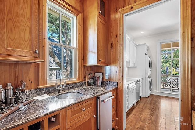 kitchen featuring wood finished floors, a sink, stainless steel dishwasher, brown cabinets, and dark stone countertops