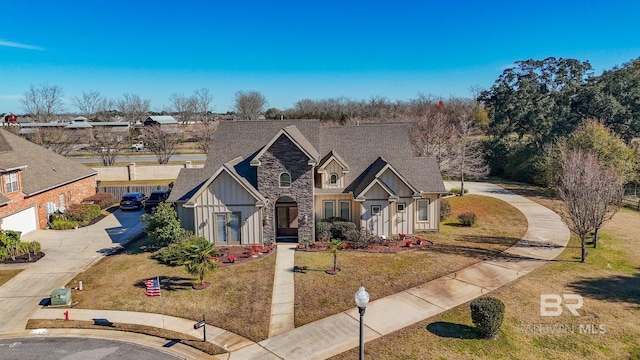 view of front of property featuring board and batten siding, a shingled roof, a front yard, stone siding, and driveway