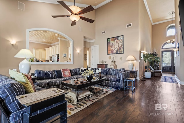 living room with ceiling fan with notable chandelier, dark wood-type flooring, ornamental molding, and a high ceiling