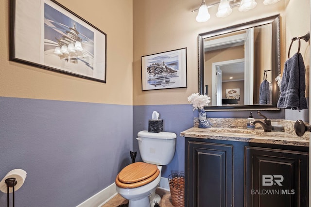 half bathroom featuring baseboards, toilet, and vanity