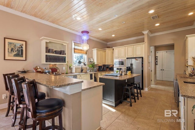 kitchen with a kitchen bar, cream cabinetry, a peninsula, appliances with stainless steel finishes, and wooden ceiling