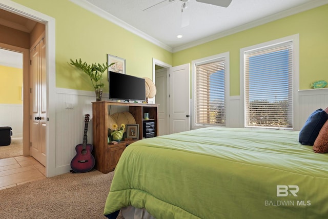 carpeted bedroom featuring crown molding, a ceiling fan, and a wainscoted wall