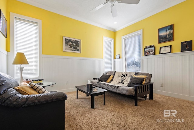 living area featuring a wainscoted wall, carpet flooring, a ceiling fan, and ornamental molding