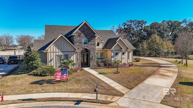 view of front of property featuring board and batten siding, a front lawn, fence, and stone siding