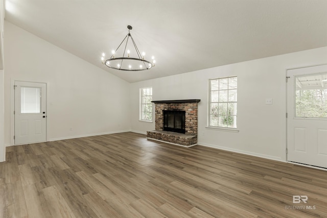 unfurnished living room with baseboards, a fireplace, wood finished floors, and an inviting chandelier