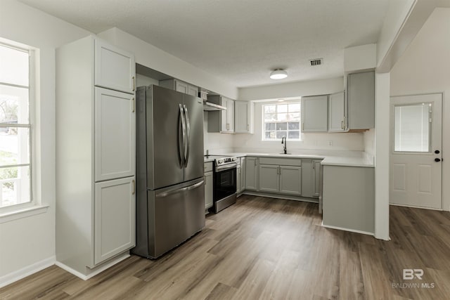 kitchen with stainless steel appliances, gray cabinets, visible vents, a sink, and wood finished floors