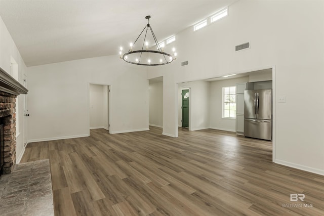 unfurnished living room featuring a brick fireplace, wood finished floors, visible vents, and a notable chandelier