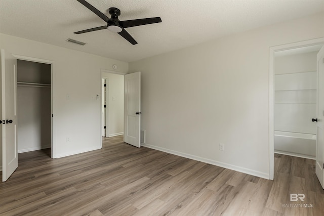 unfurnished bedroom featuring visible vents, a walk in closet, a closet, and wood finished floors