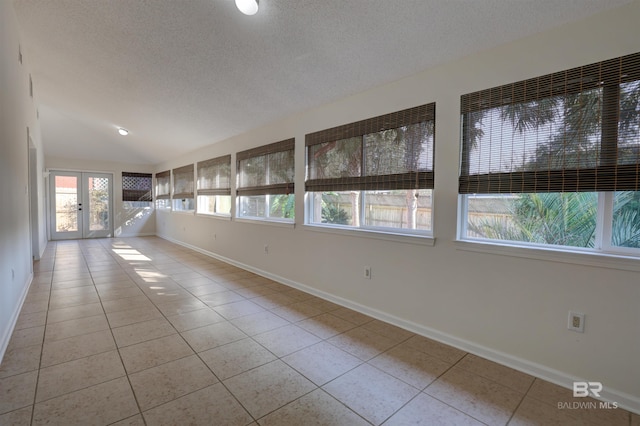 tiled spare room with lofted ceiling, french doors, and a textured ceiling