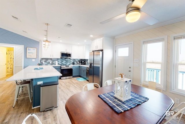 dining area featuring visible vents, light wood-style flooring, crown molding, and a ceiling fan