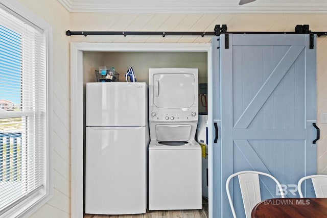 laundry area with a barn door, ornamental molding, laundry area, stacked washer and clothes dryer, and wood finished floors