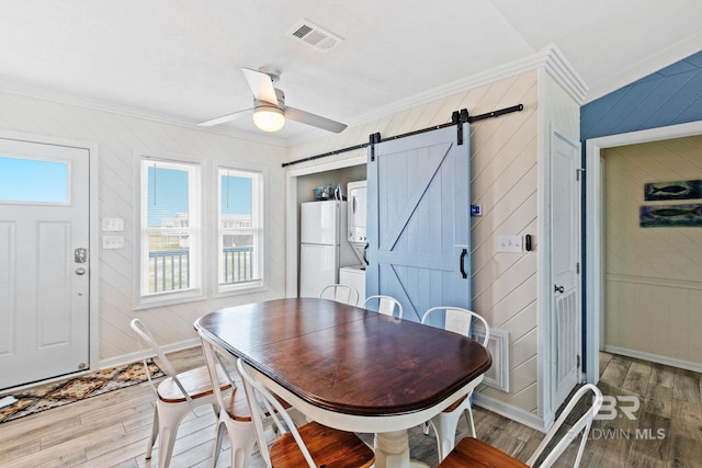 dining area with a barn door, ornamental molding, light wood-style floors, and stacked washing maching and dryer