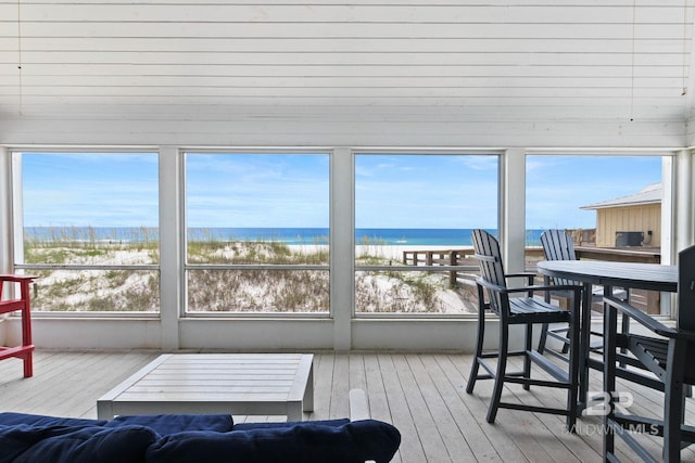 sunroom featuring plenty of natural light, a beach view, and a water view