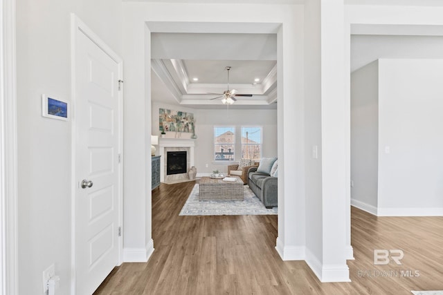 living room with a tray ceiling, ceiling fan, light hardwood / wood-style floors, and ornamental molding