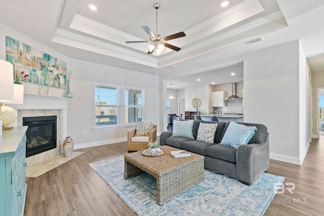 living room featuring a tray ceiling, ceiling fan, a high end fireplace, and light wood-type flooring