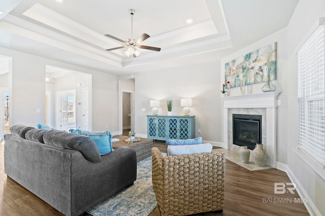 living room with a raised ceiling, ceiling fan, a high end fireplace, and dark hardwood / wood-style floors