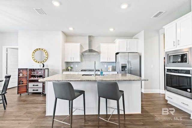 kitchen with white cabinets, stainless steel appliances, light stone counters, and wall chimney exhaust hood