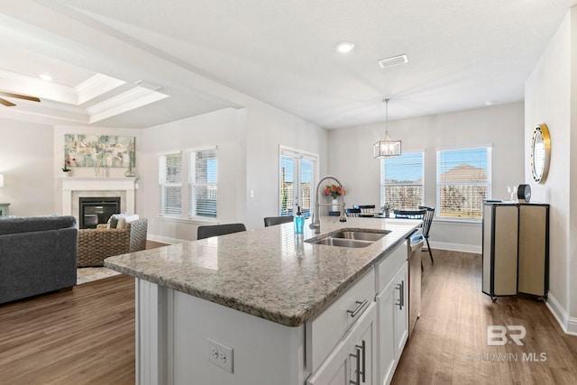 kitchen featuring white cabinets, a center island with sink, sink, hanging light fixtures, and light stone countertops