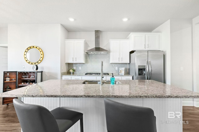 kitchen with light stone counters, white cabinets, stainless steel appliances, and wall chimney range hood