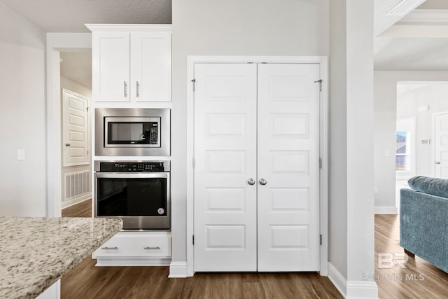 kitchen featuring light stone countertops, white cabinets, dark wood-type flooring, and appliances with stainless steel finishes