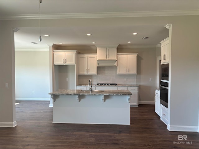 kitchen featuring white cabinets, gas stovetop, light stone counters, and a kitchen island with sink