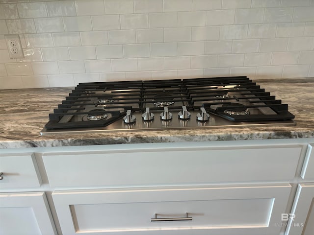 room details featuring white cabinetry, dark stone countertops, decorative backsplash, and stainless steel gas cooktop