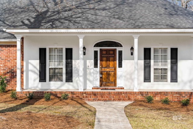 property entrance with covered porch, roof with shingles, and brick siding